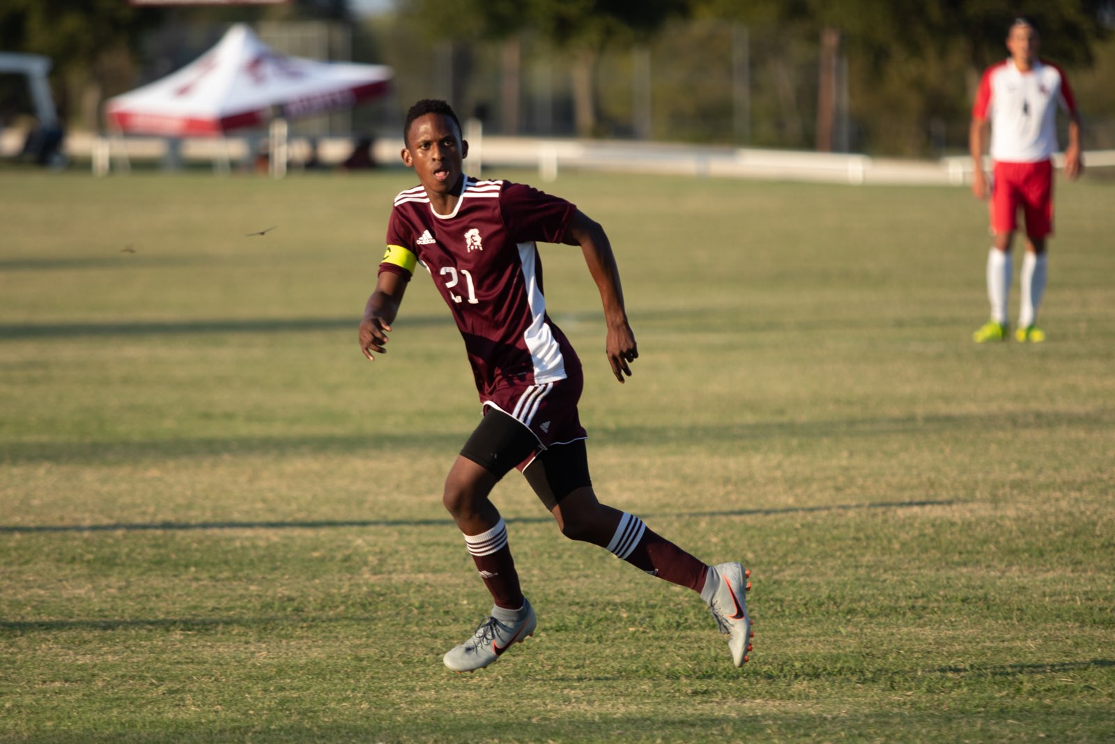 A soccer player in unifrom runs acrross the field during a game and is very focused