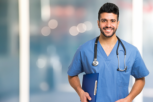 A nurse smiles as he wears blue scrubs along with a stethoscope around his neck smiles 