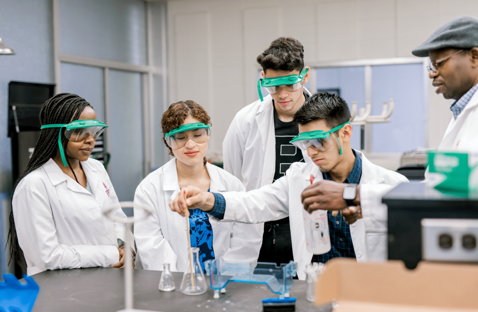 A student begins to mix something in a flask as his peers and professor stand around in observation.
