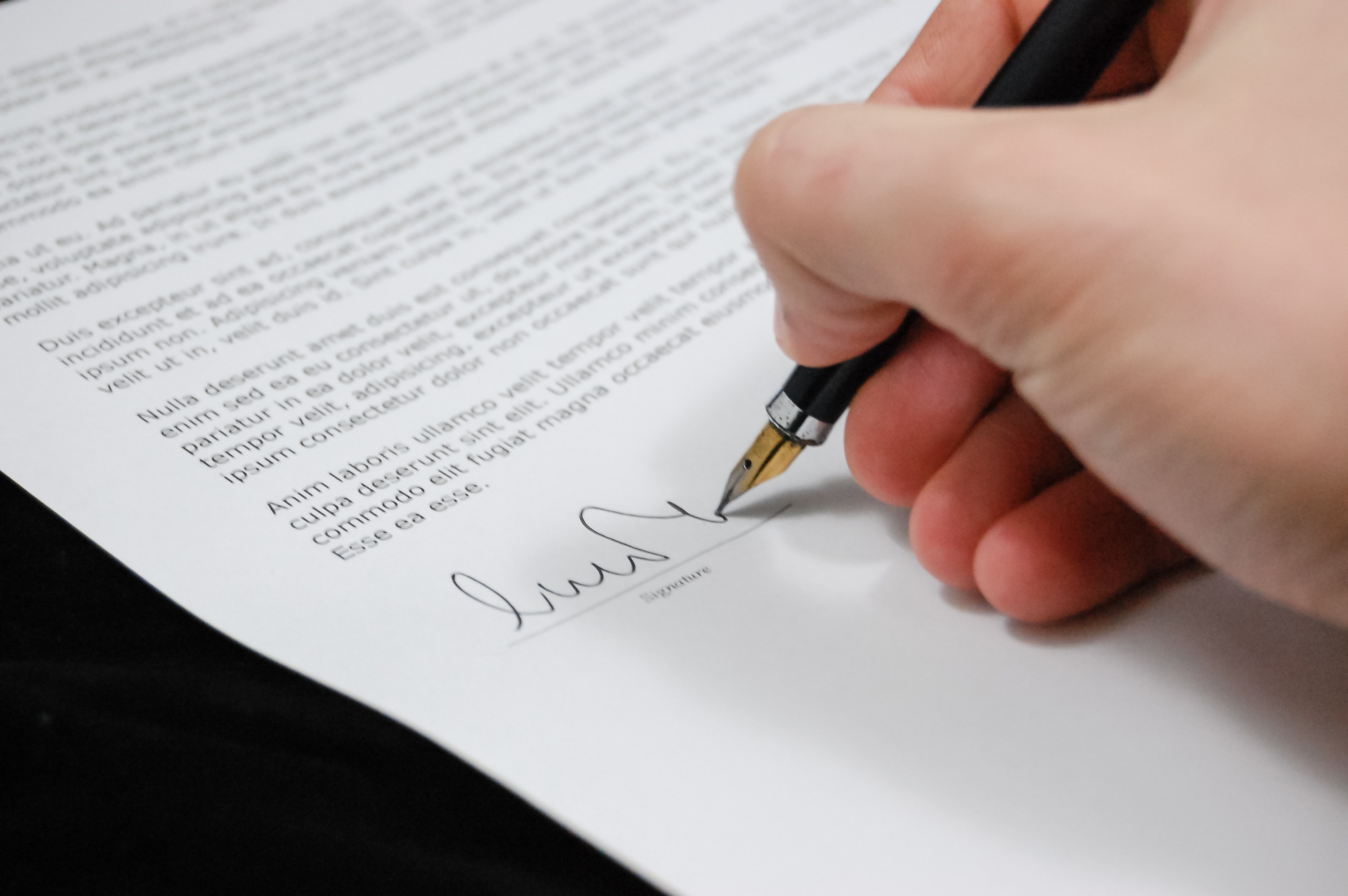 Hand holding pen, signing at the bottom of a document
