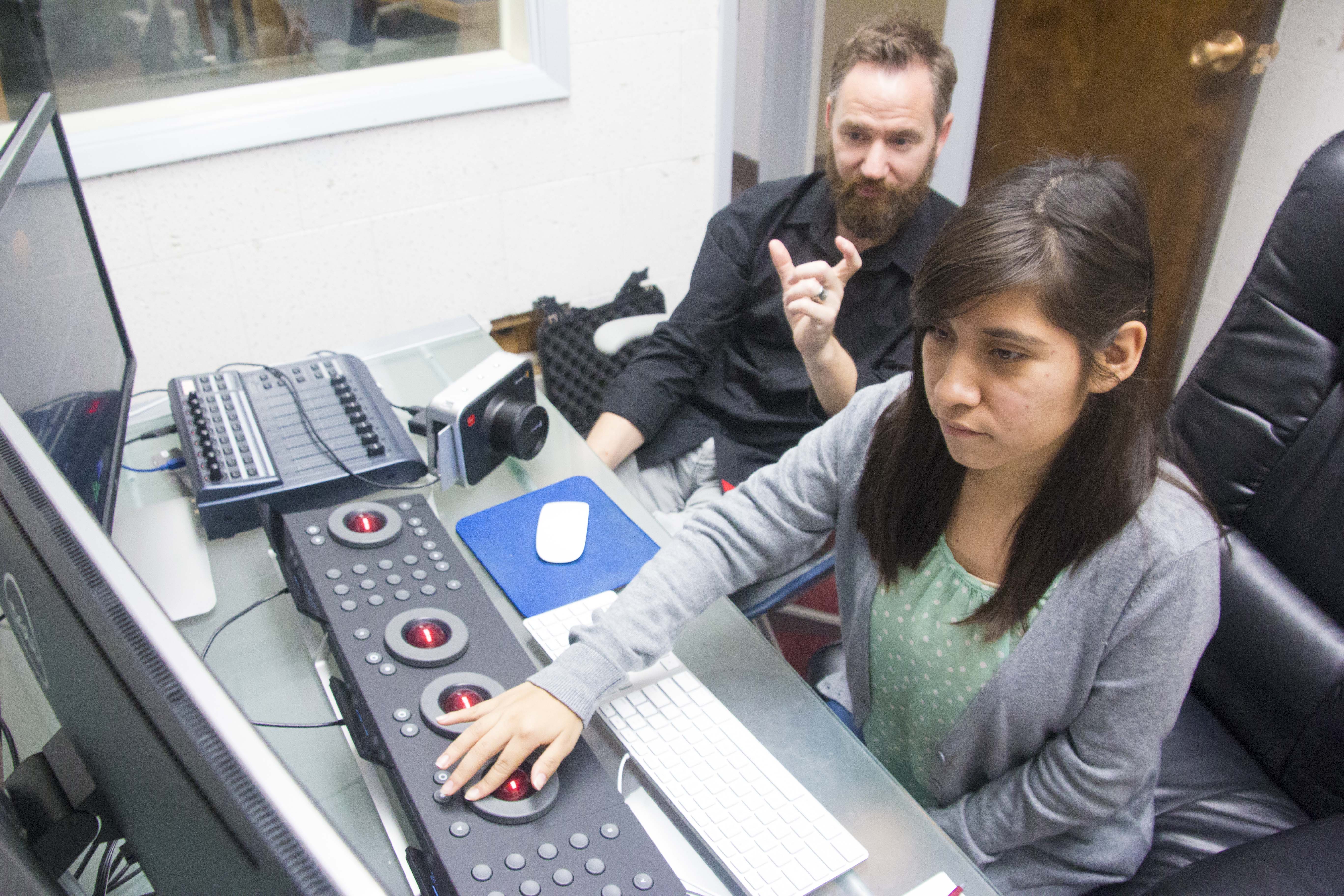 Sitting in front of a keyboard of buttons and balls, a student makes adjustments as she looks at two screens.