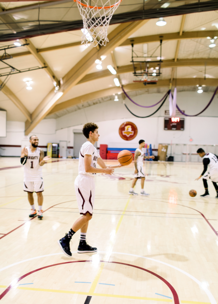 A group of basketball players in uniform practice and throw the ball around at the gymnasium