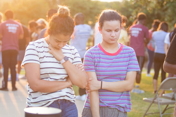Two students stand near each other and bow their heads to pray.