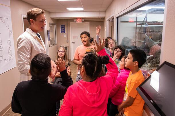 Excited kids begin to raise their hands as they answer questions about the dinosaur bone in front