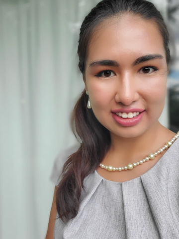 A young woman smiles as she wears pearls and a gray business professional top