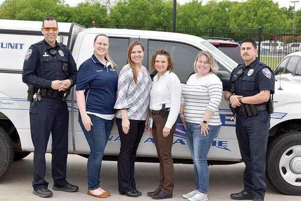 Four women stand in between two officers in uniform and smile in front of a truck