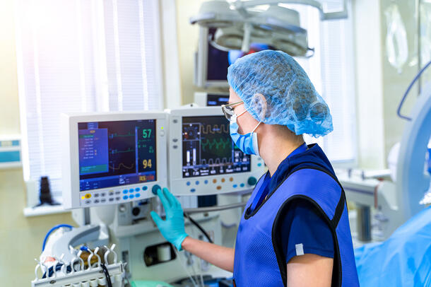 A female nurse, wearing a protection vest, gloves, and masks places her hand on a monitor