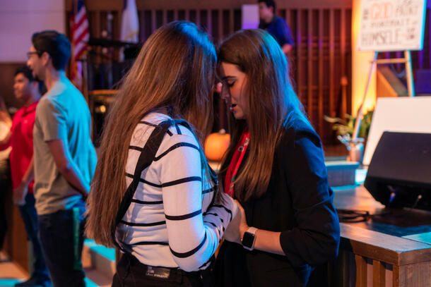 In the Keene Church, two female students hold hands and bow their head as they pray together