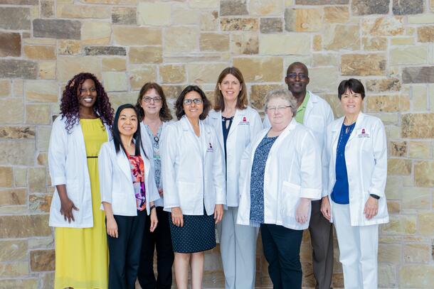 Seven members of the nursing faculty proudly wear their white coats as they stand side by side and smile