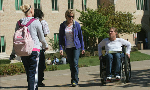 A girl in a wheelchair talks to her friend and they head towards class together