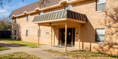 The exterior of Meier Hall which is made of light tan bricks and a brown roofing with a small covering in front of the door 