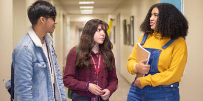 A group of three students stop in a hallway as the talk to each other