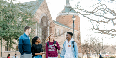 Four students stand togther outside of Pechero while they smile at each other. 