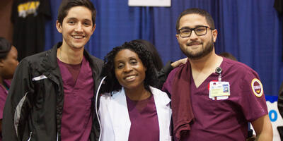 Three people dressed in SWAU scrubs pose in front of navy blue curtain