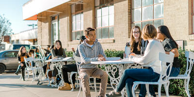 Outside several students are sitting with their friends at the metal tables and chairs outside of the Student Center