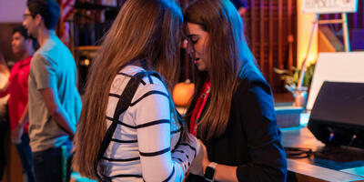In the Keene Church, two female students hold hands and bow their head as they pray together