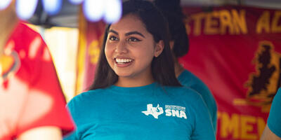 A nursing student, dressed in her blue club shirt, smiles as she explains the nursing club to another student