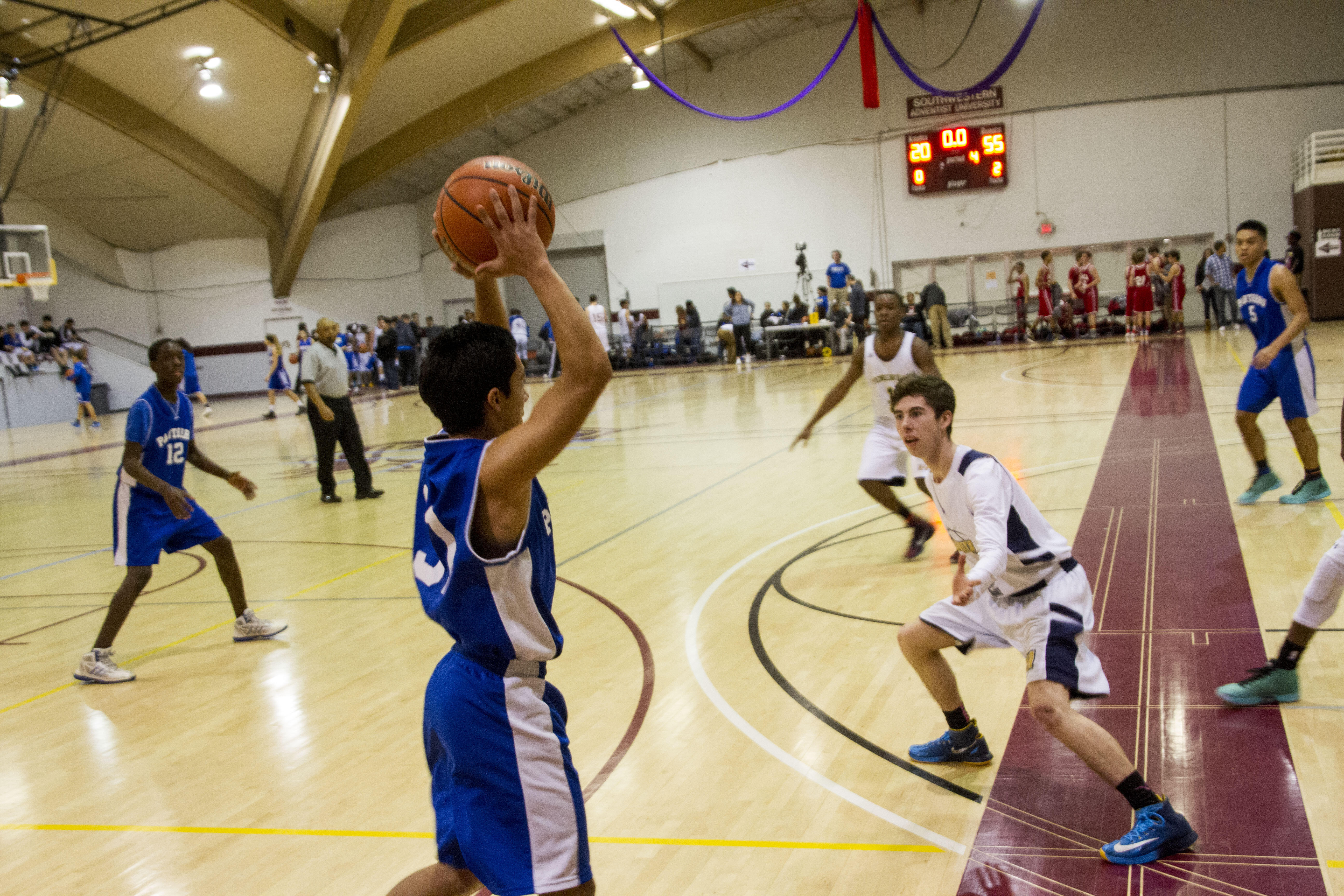 A high school basketball player holds the ball over his head as he looks to see who is open