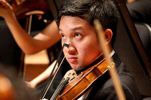 A violinist begins to play while look at the conductor for his cue.