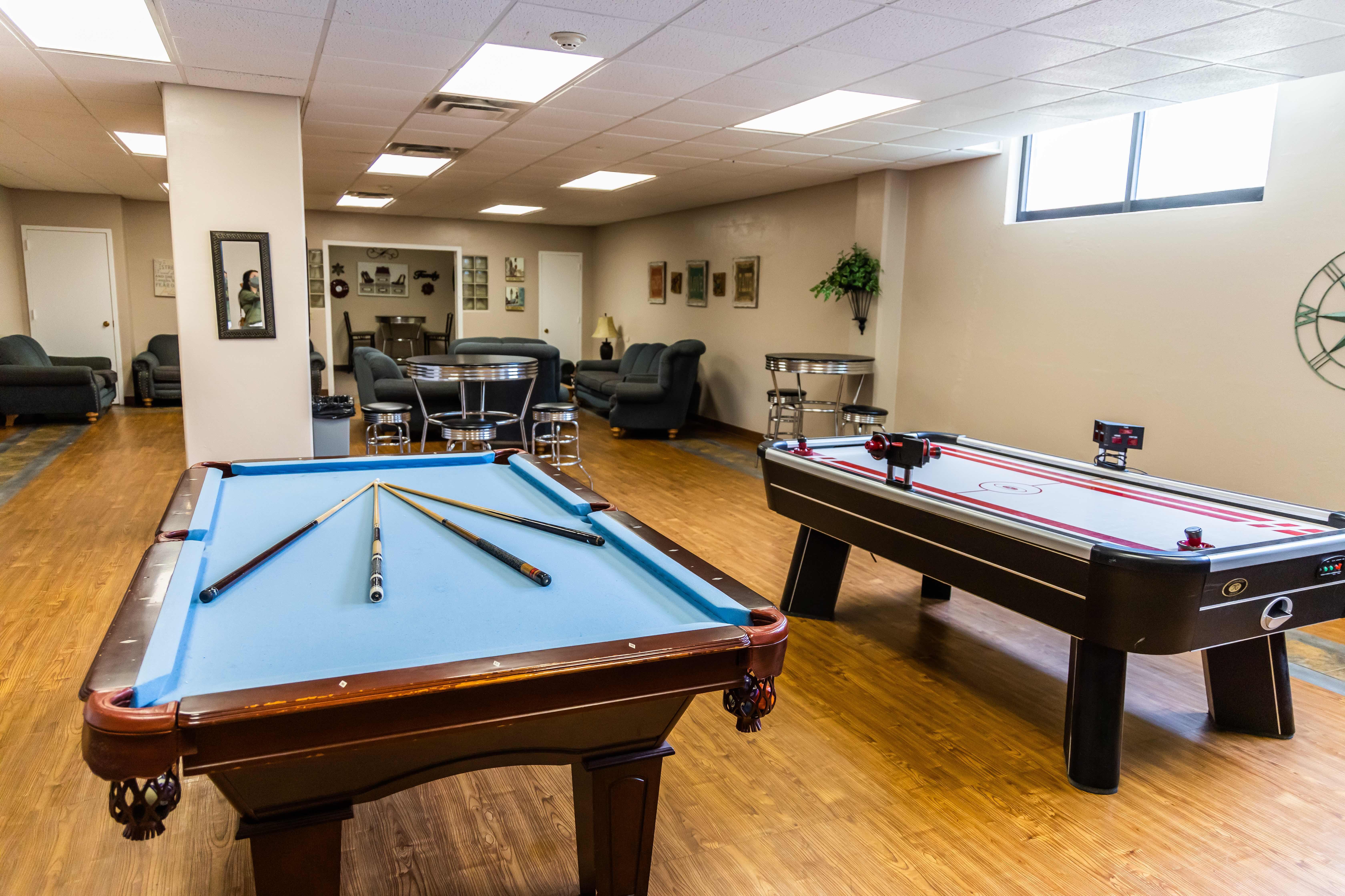 A game room with a pool table, air hockey table and various couches for seating