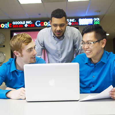 Three students sit around a laptop as they discuss their business strategy