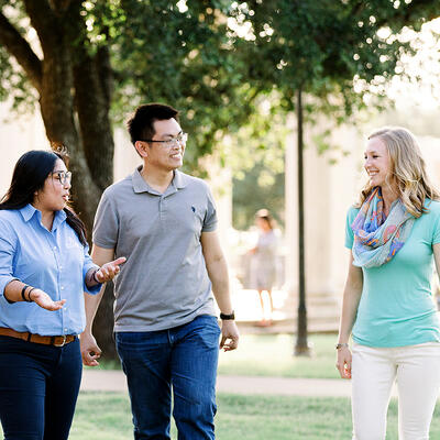 While walking through campus, small groups of alumn smile as they talk outside