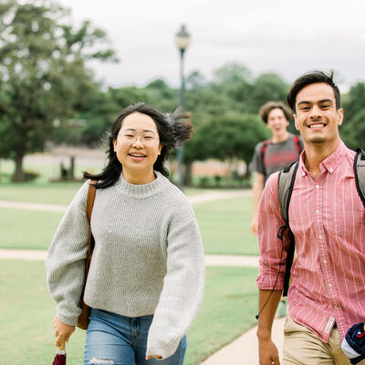 Two students look up and smile as they walk together on campus