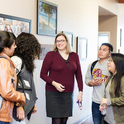 A female professor stands amongst her students and they discuss their class topics