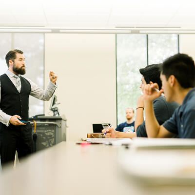 Dressed in business professional clothes, a professor teaches the students in front of him
