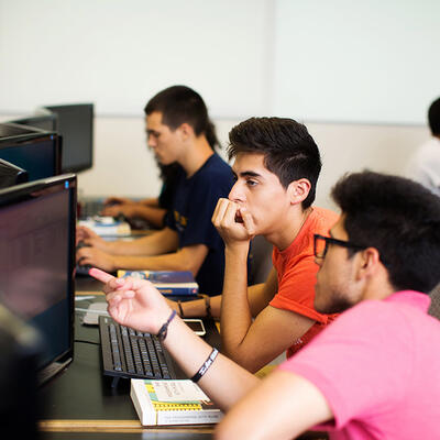 A student leans over as he helps his peer in their computer science class