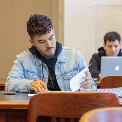 A student sits at the library table and flips through some papers as he studies