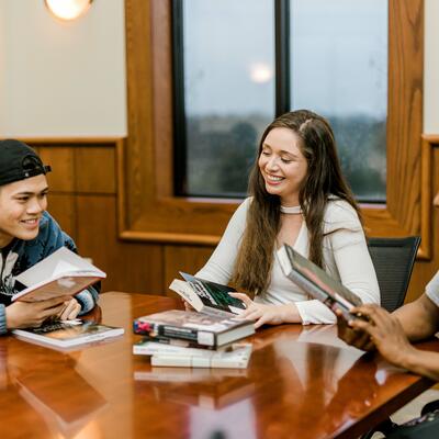 Three students sit together in a table in pechero smiling and looking through books