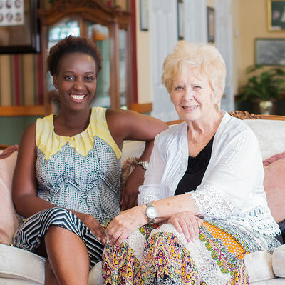 Sitting on a white couch and chair, three women look forward and smile