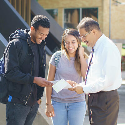 Students speaking with a professor and reviewing paperwork with students outside