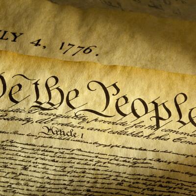Two old documents with a yellow tint read the beginning words of the constitution