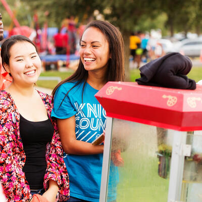 Two students smile and laugh as they wait in front of the popcorn machine