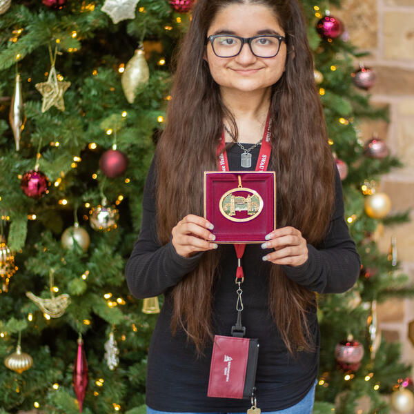 Caroline Torres poses in front of a Christmas tree holding a box containing the Mizpah ornament