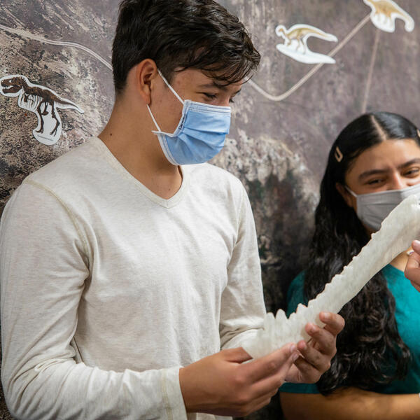 Student holds white dinosaur bone replica in Dinosaur Science Museum while standing next to another student