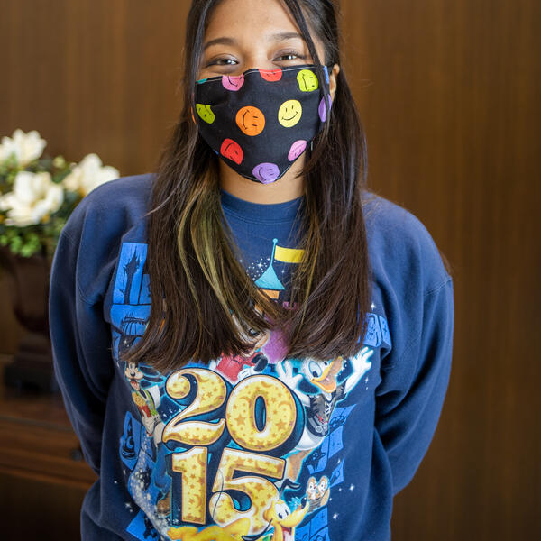 Genesis Santos poses for the camera in a mask with cartoon smiling faces and a blue sweatshirt