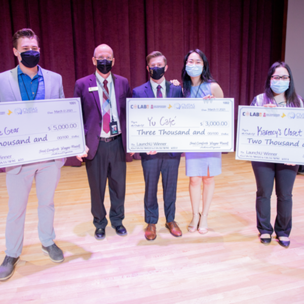 Dr. Shaw stands with the winners of the LaunchU competition who are all holding large checks that say the amount of money they have won