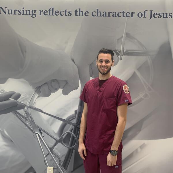 Male nurse student smiles as he stands in his maroon scrubs 