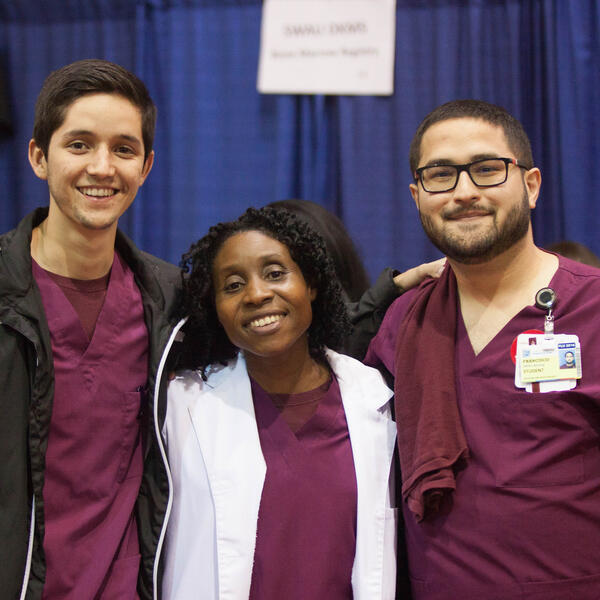 Three people dressed in SWAU scrubs pose in front of navy blue curtain