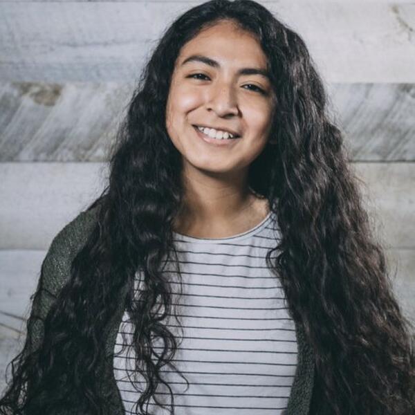 Headshot of Samantha-Lee against a wood background in a black and white striped shirt and a green cardigan