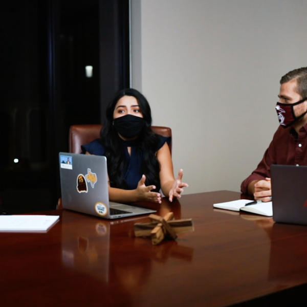 Three people wearing masks sit around a table with computers having a conversation