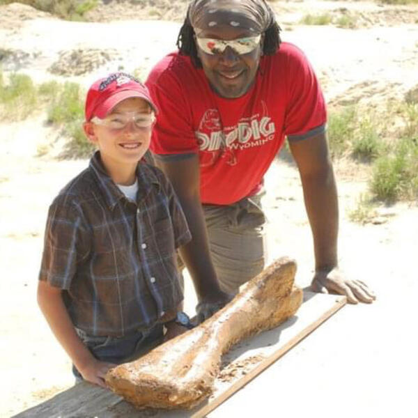 Stephan Gray and a young boy stand next to a dinosaur bone laying on a table