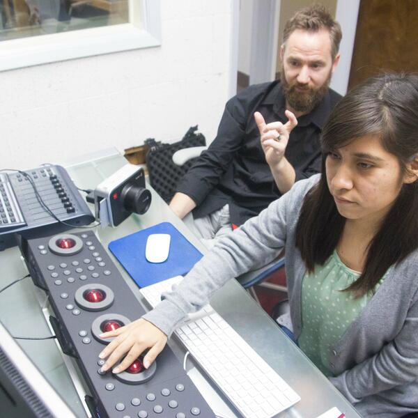 Sitting in front of a keyboard of buttons and balls, a student makes adjustments as she looks at two screens.