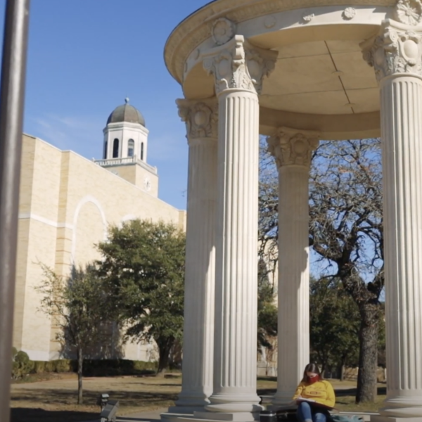 Student in yellow shirt sits at the rotunda with the library in the background