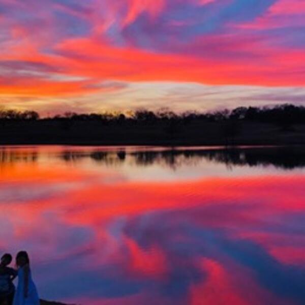 Reflecting off of a pond, the sun sets with bright colors of yellow, orange, pink, blue and purple