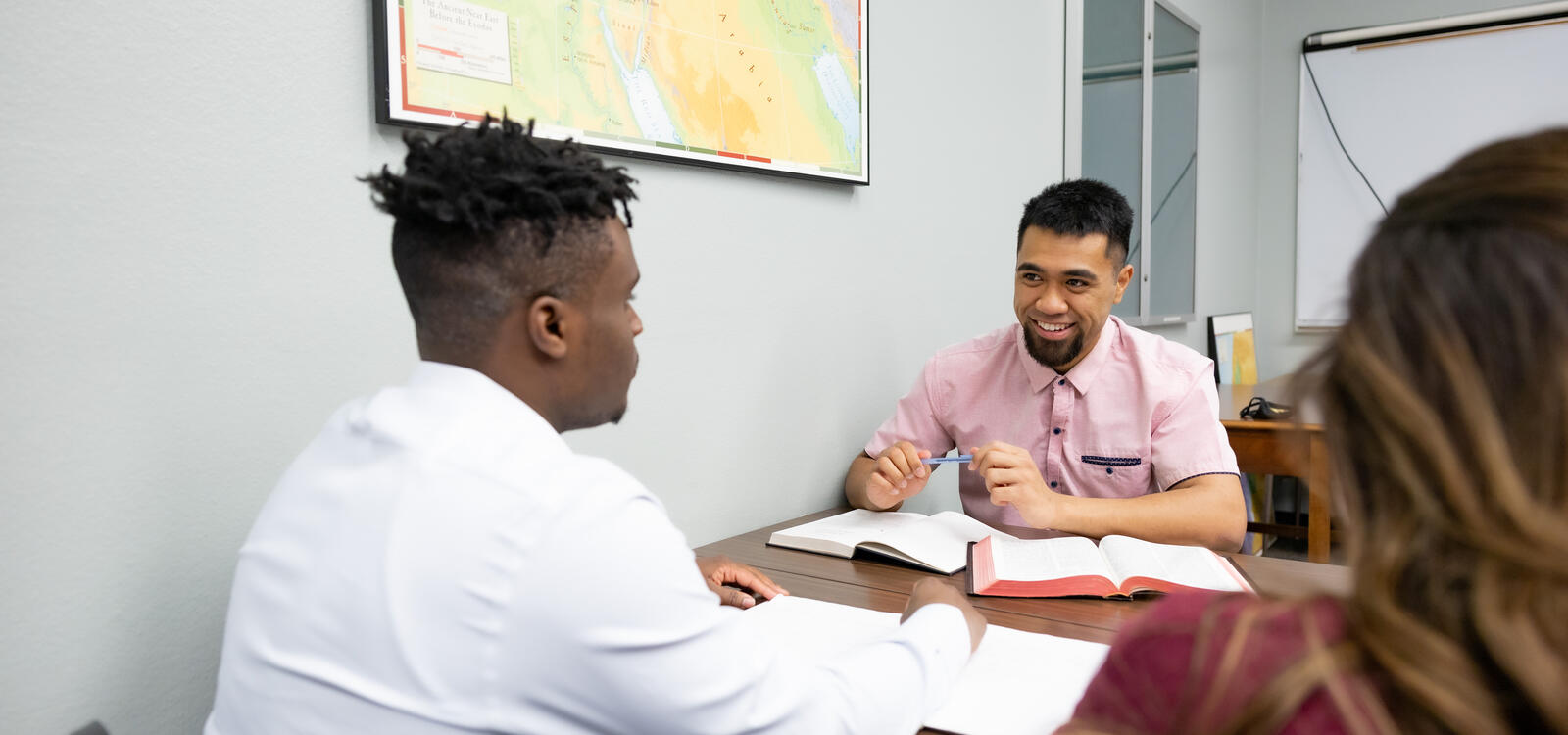 A male student smiles at another male student as they study the bible together.