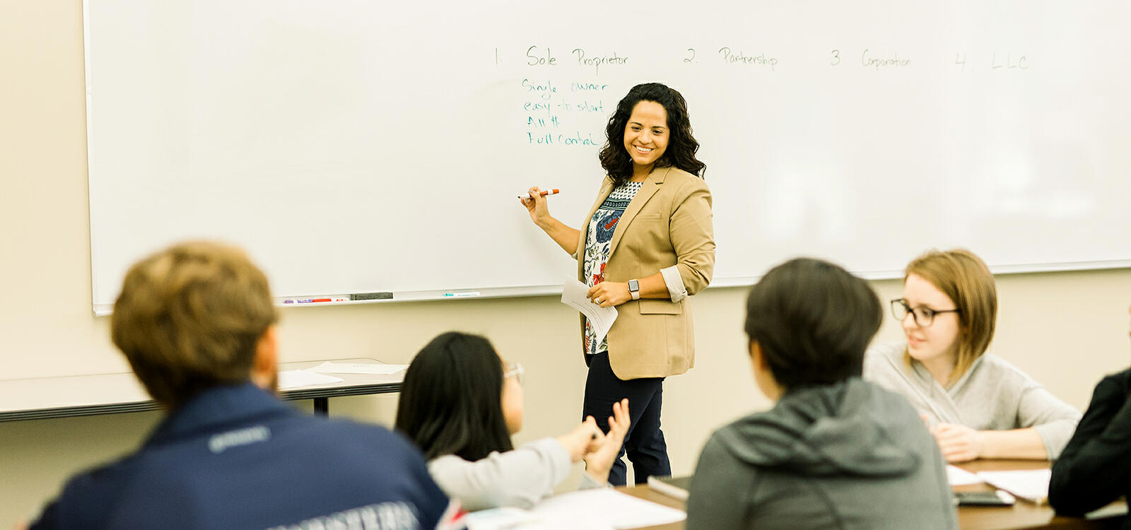 A business professor smiles and turns from writing on her board as she listens to a students question